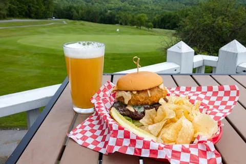 burger on outdoor table with beer and golf course in background