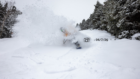 Snowboard in a yellow jacket slashing powder