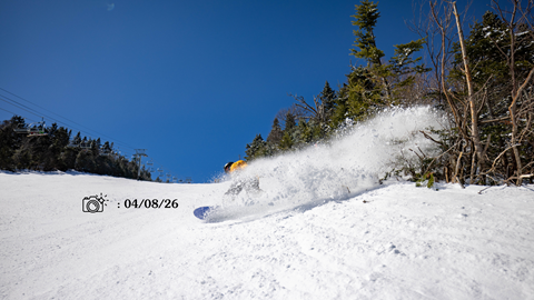 Snowboarder in a yellow jacket on a sunny day carving snow