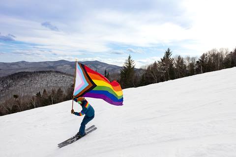 Skier skiing with a pride flag down Spring Fling
