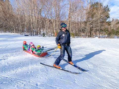 ski patrollers gives little kids a toboggan ride