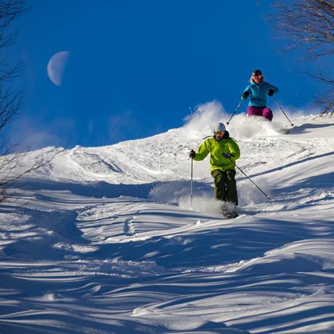 Skiers ripping powder under the moon
