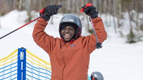 Smiling skier celebrating with raised poles on a snowy slope at Sugarbush Resort.