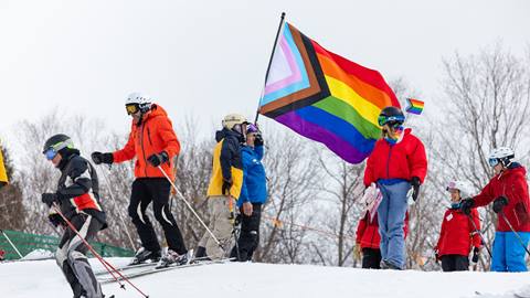 Skiers and riders gathered on a snowy slope at Sugarbush holding a large Progress Pride flag.