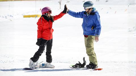 A student and instructor high fiving while snowboarding