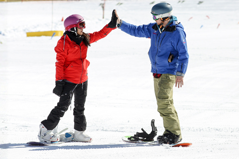 A student and instructor high fiving while snowboarding