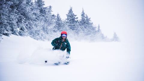 A skier in a green jacket ripping down a trail on a powder day.