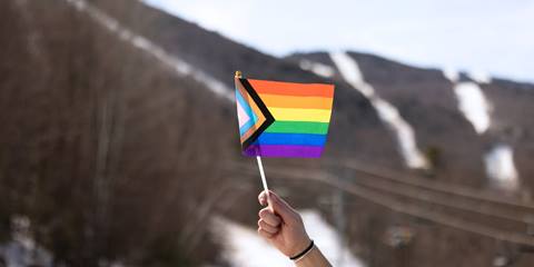 hand holding small pride flag with sugarbush mountain in the background