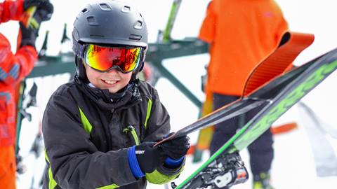 A kid pulling ski skins apart and smiling at the camera