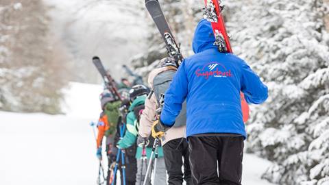 An instructor and kids hiking up a ski slope with skis on their shoulders