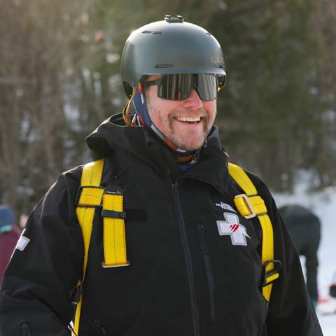 A ski patroller wearing a full body harness and helmet smiling at the camera. 