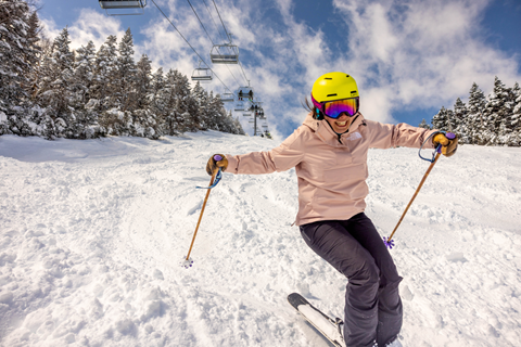 A woman in a pink jacket smiling and skiing down Ripcord on a powder day. 