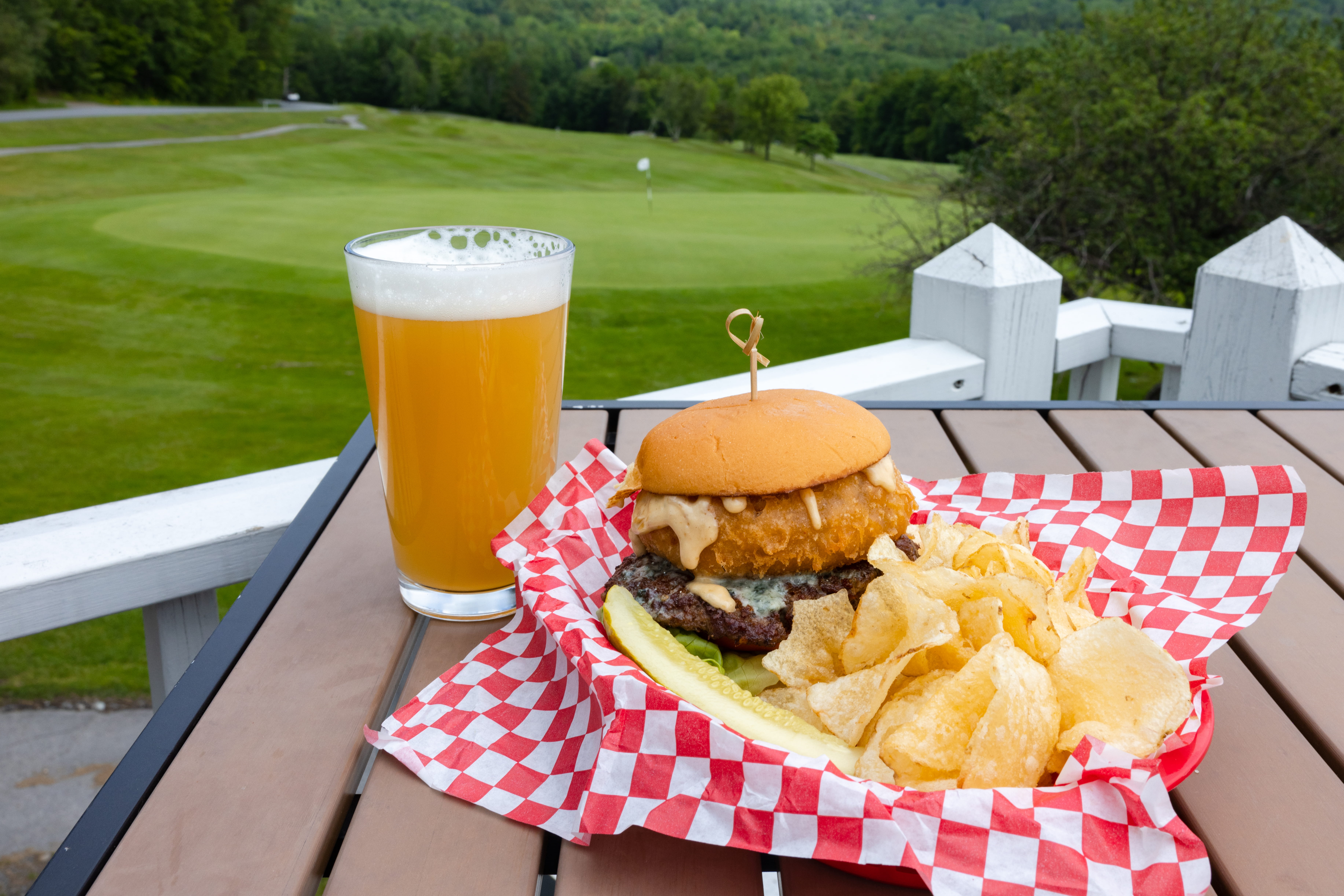 burger on outdoor table with beer and golf course in background