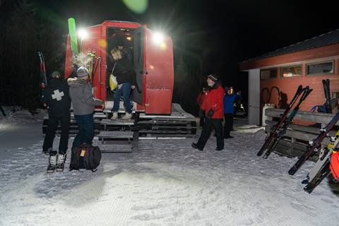 A group of people standing around outside a snowcat at night