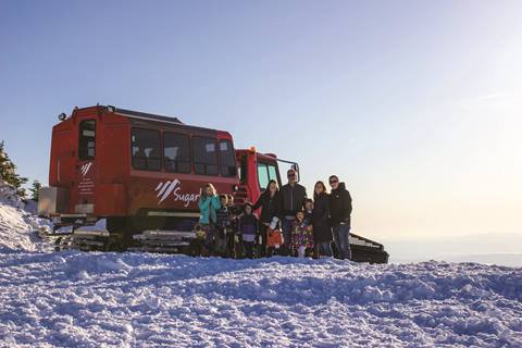 Group of people standing in front of a snowcat on snowy ski trail
