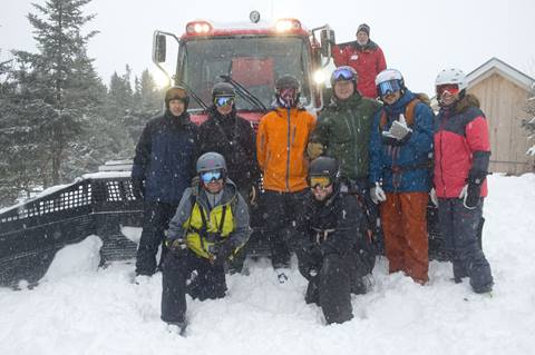 Group of people in front of a snowcat on a snowy ski trail