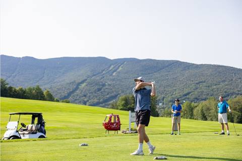 golfer swings with group watching and mountain view