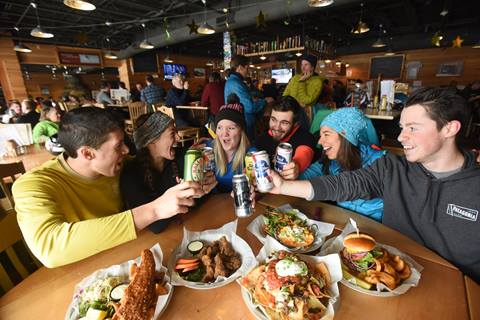Group of people sharing a drink at a table covered with plates of food in the Castlerock Pub at Sugarbush Resort