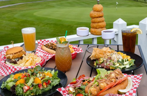 Table full of plates of food on a deck overlooking a golf course