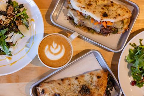 Close up top down shot of a table full of plates of food and a latte