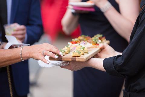 Close up of a person grabbing food from a waiter holding a serving tray