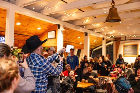 Person shooting a champagne cork at a cowbell in a cowboy hat