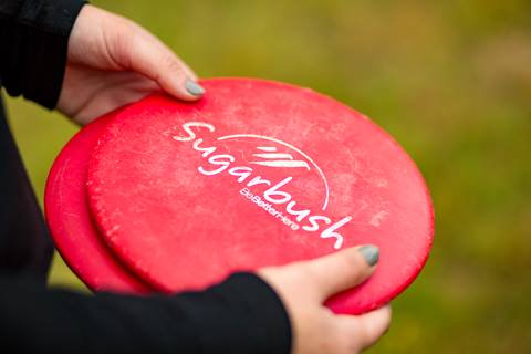 Close-up of a person holding a Sugarbush Resort branded disc against an outdoor background.