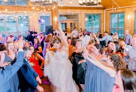 Bride dances with wedding guests at reception under string lights