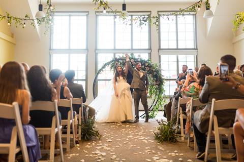 Bride and Groom celebrate under arbor at indoor ceremony